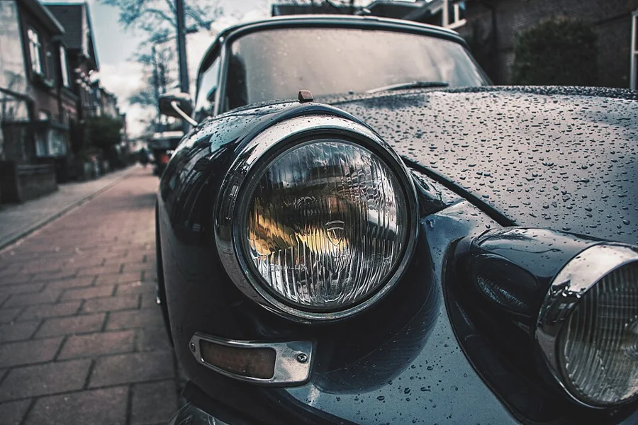 Round headlight of a dark car wet with rain