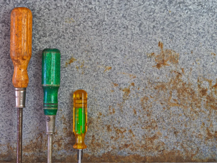 Three screwdrivers leaning against a metal wall